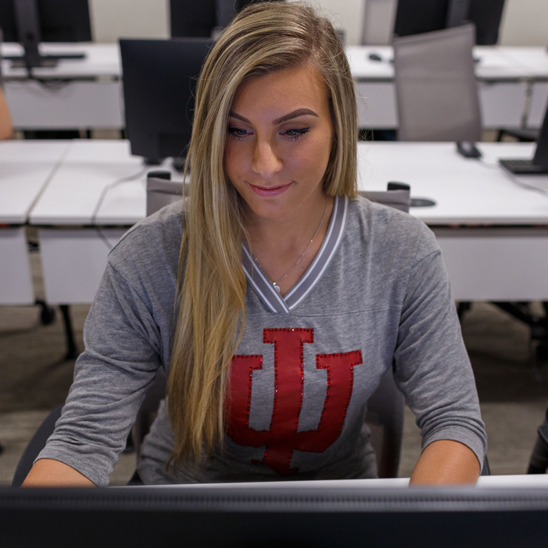 A woman wearing a shirt with the IU trident looking at a computer.